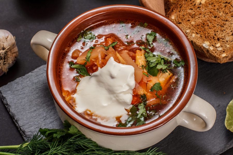 Ukrainian traditional borsch in porcelain bowl with sour cream, rye bread on black stone board. Top view.